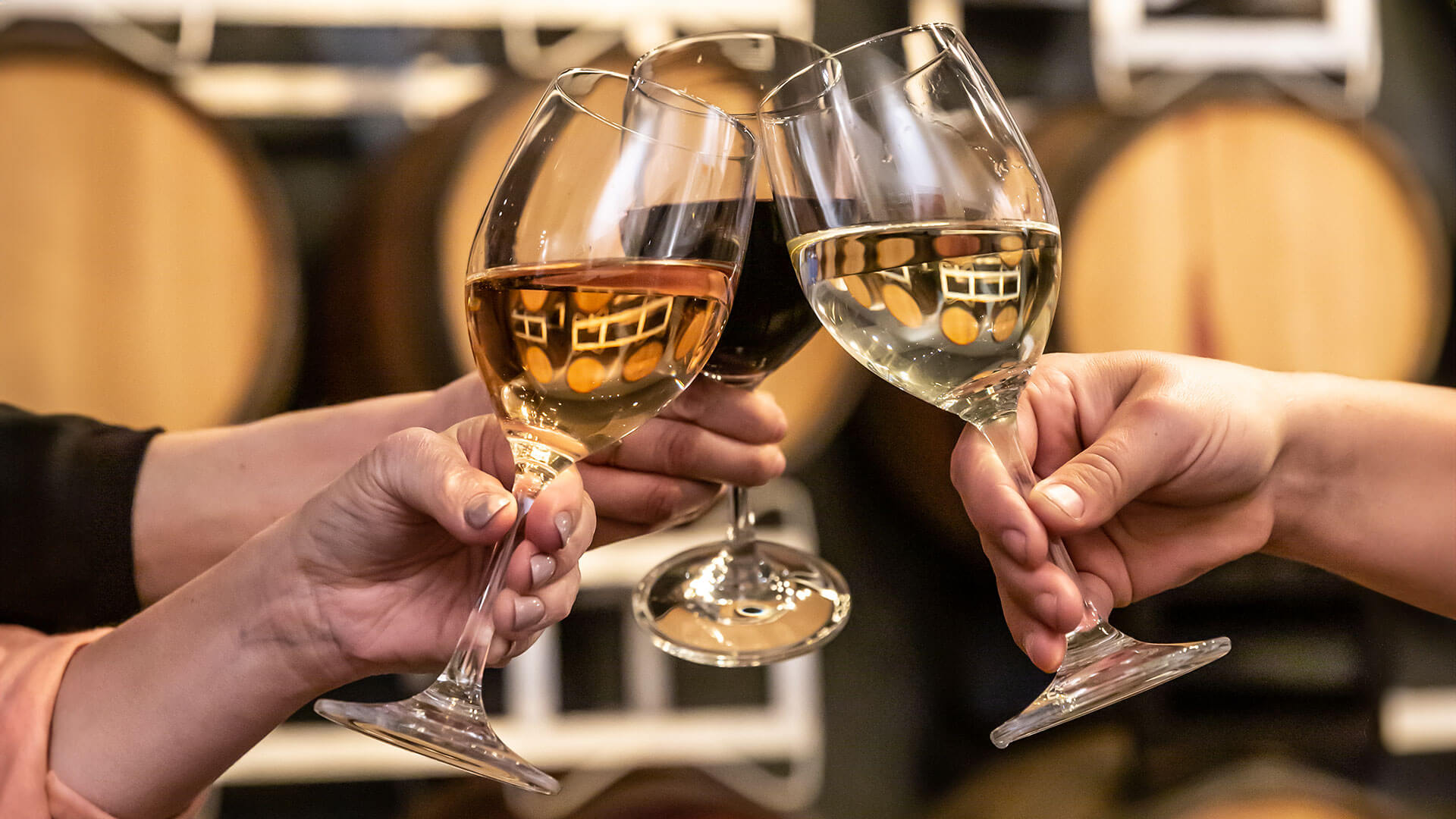 Red, White and Rose wine toasting in front of wine barrels.