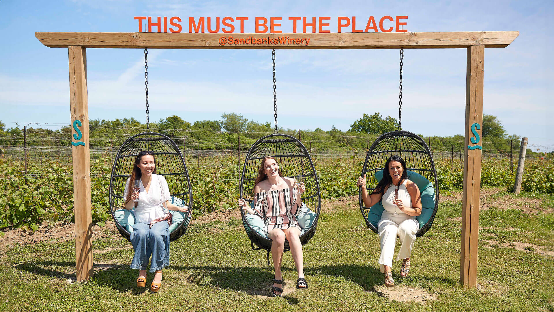 Friends enjoying the Sandbanks Winery with a glass of wine on a swingset.