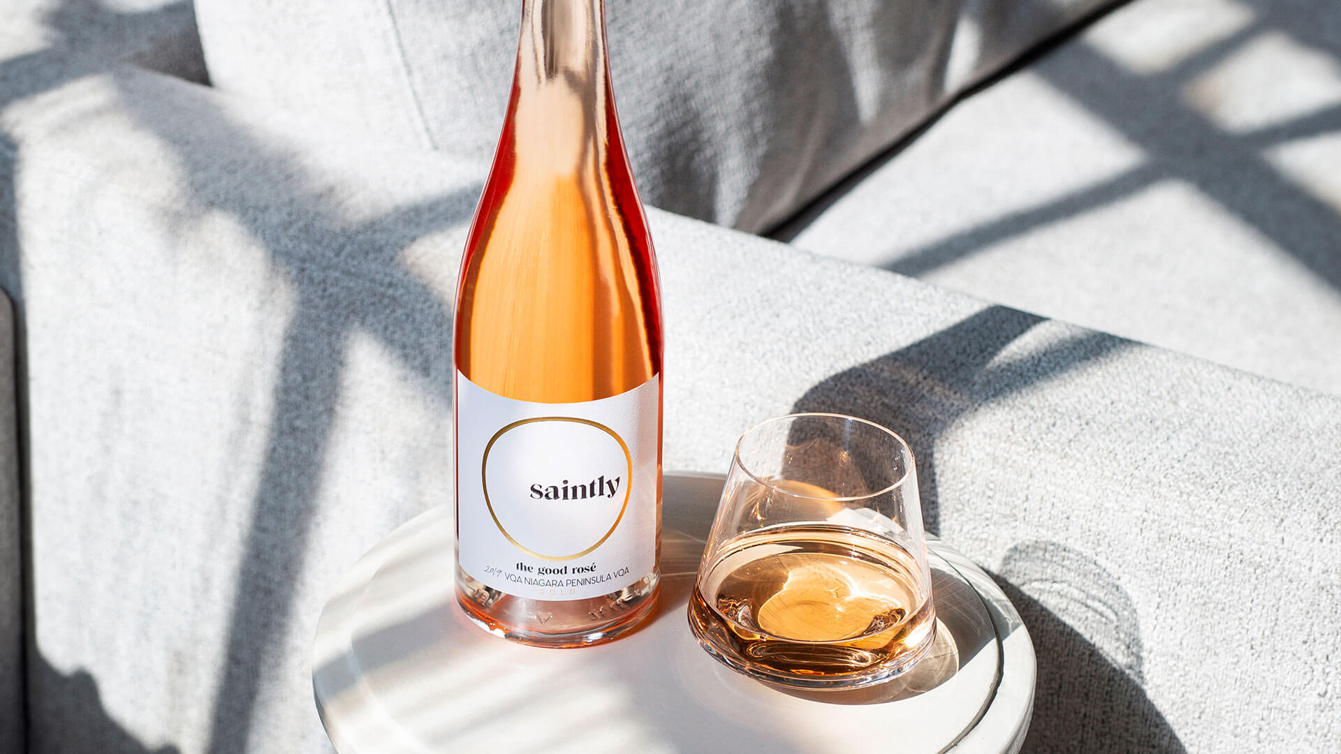 Bottle and glass of Saintly Rosé on a sidetable near couch.